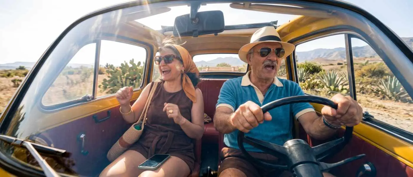 An older couple laughing in a vintage yellow car on a desert road.